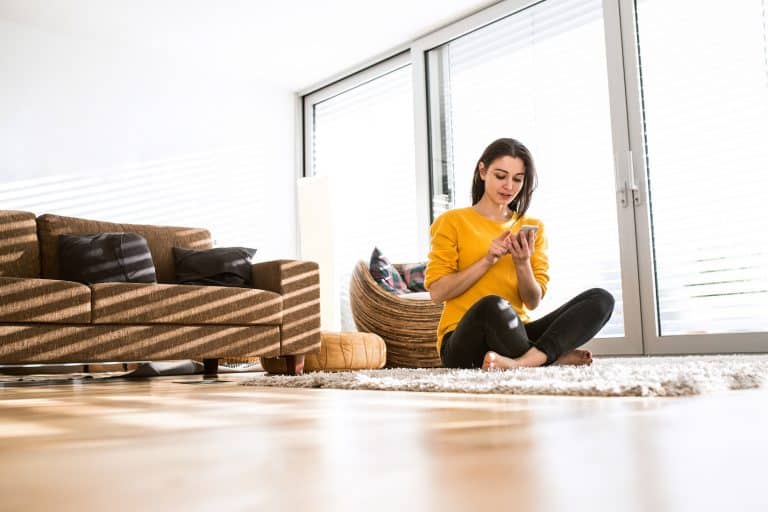 Woman at home sitting on carpet, holding smart phone, texting